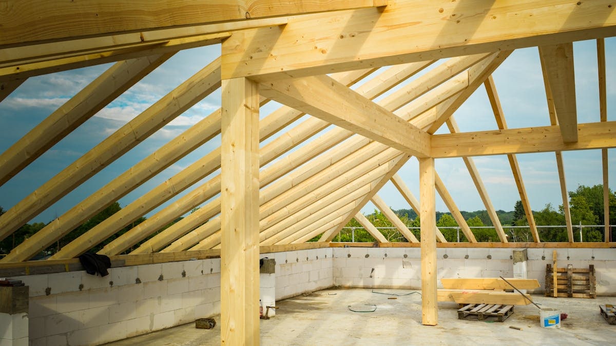Unfinished construction site with a focus on wooden roof trusses under a clear sky.